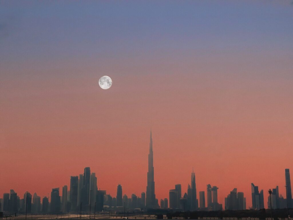 Downtown Dubai skyline silhouette at dusk with full moon, near Dubai Islands
