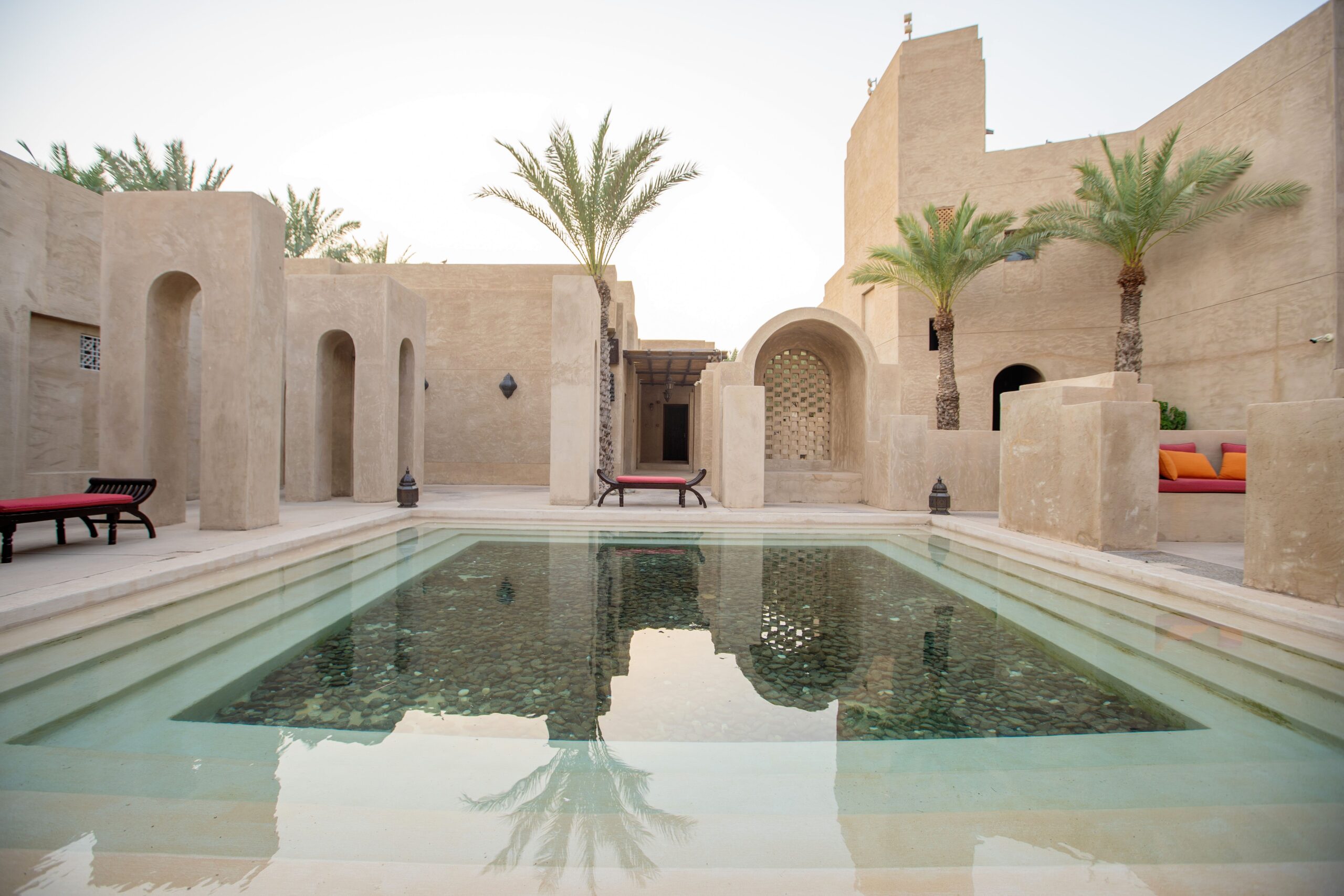 Sandstone Arabian-style courtyard with a reflecting pool and palm trees, representative of Al Muntazah Complex's low-rise gated villa community in Jebel Ali Village