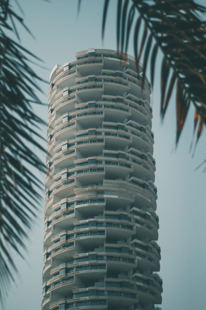 Curved balcony architecture of a modern Dubai high-rise framed by palm leaves against a clear blue sky
