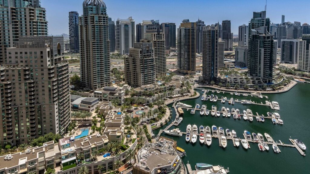 Aerial view of Dubai Marina's dense skyline of high-rise towers overlooking a marina lagoon lined with docked yachts