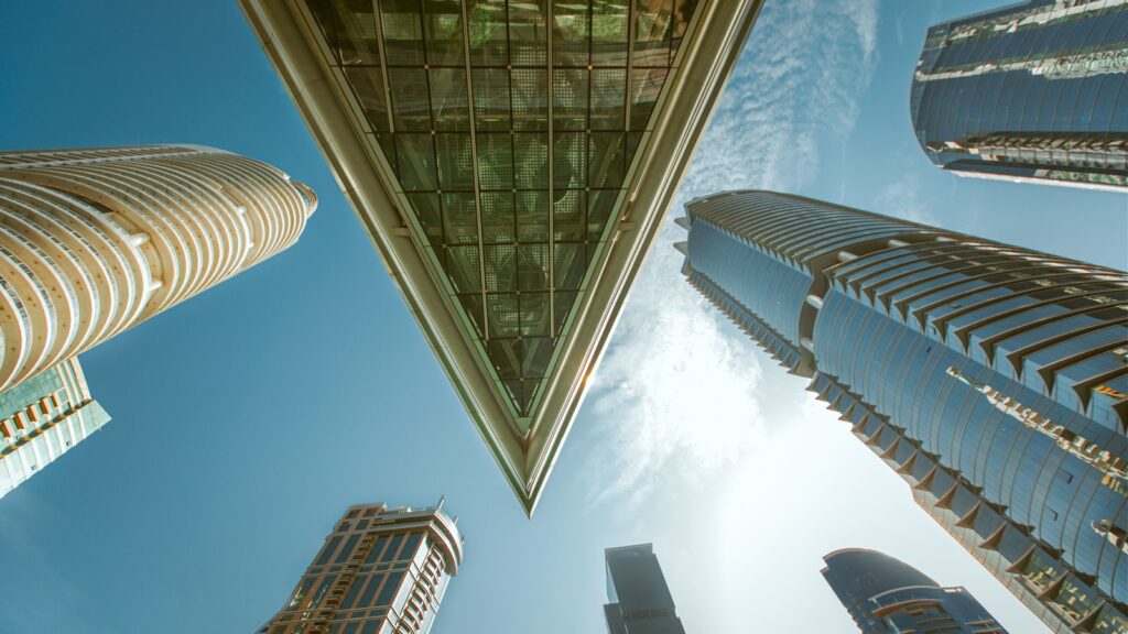Dramatic low-angle view looking straight up at Jumeirah Lake Towers skyscrapers including the triangular Almas Tower against a blue sky