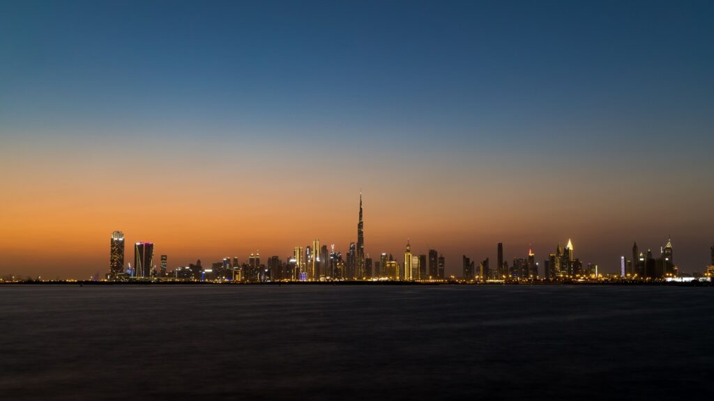 Dubai skyline at dusk with the Burj Khalifa silhouetted against an orange sunset over the water, representing Safeer Tower 1's Business Bay setting