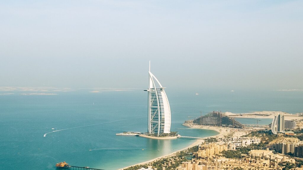 Aerial view of the Burj Al Arab with Palm Jumeirah visible on the horizon along the Dubai coastline