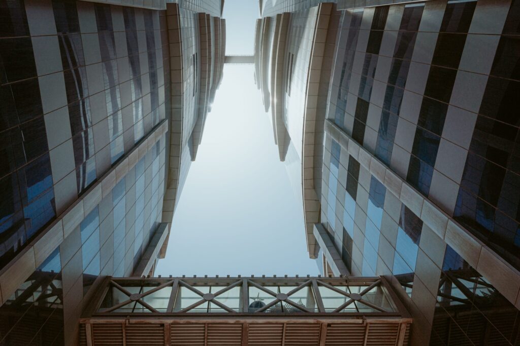 Upward view of twin glass and stone towers linked by an angled sky bridge in Business Bay, Dubai