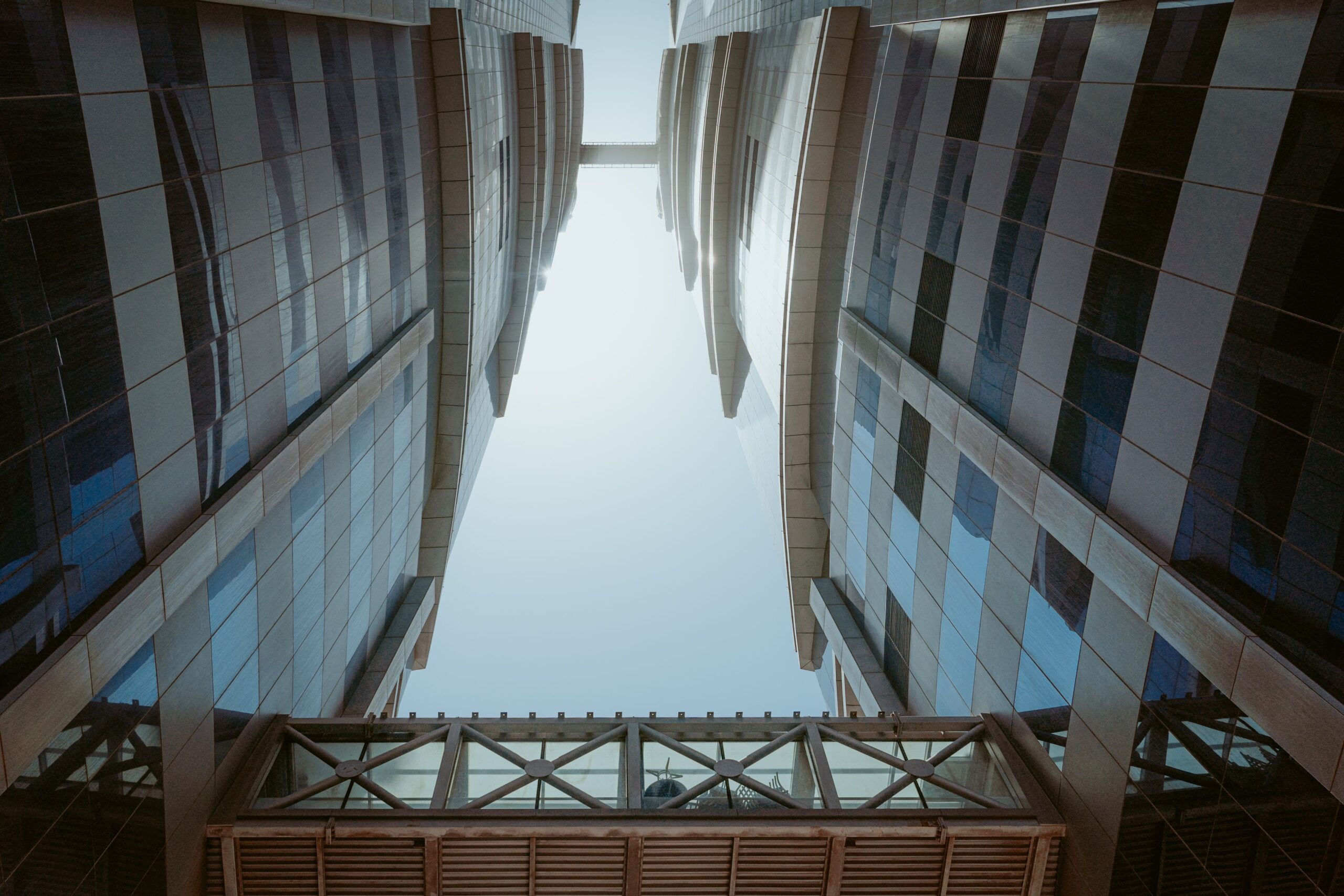 Upward view of twin glass and stone towers linked by an angled sky bridge in Business Bay, Dubai