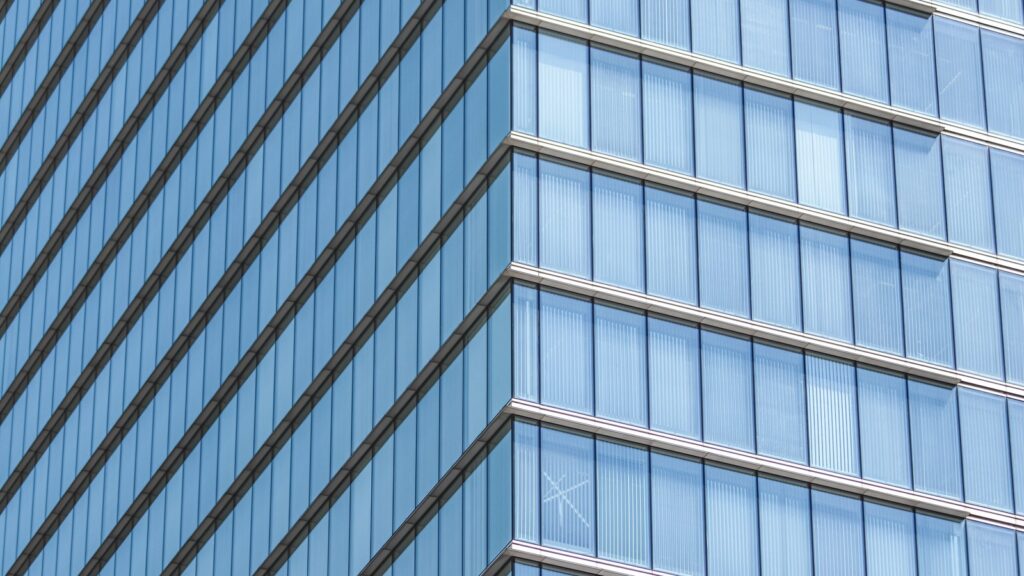 Close-up view of a modern blue glass high-rise facade with diagonal architectural lines against the sky, representing The Pad by Omniyat's Business Bay tower setting