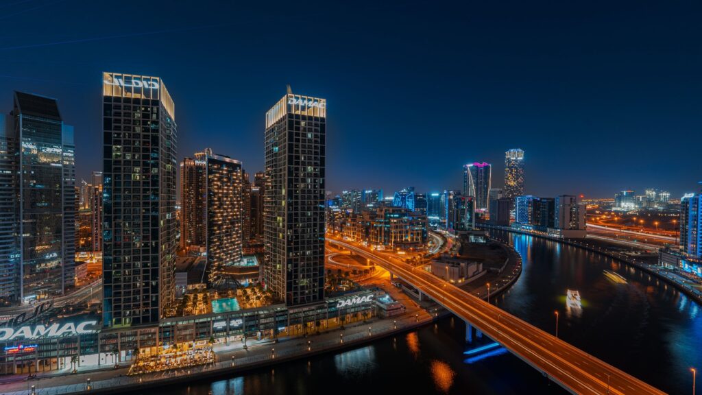 Night view of illuminated Business Bay skyscrapers along the Dubai Water Canal with a lit bridge