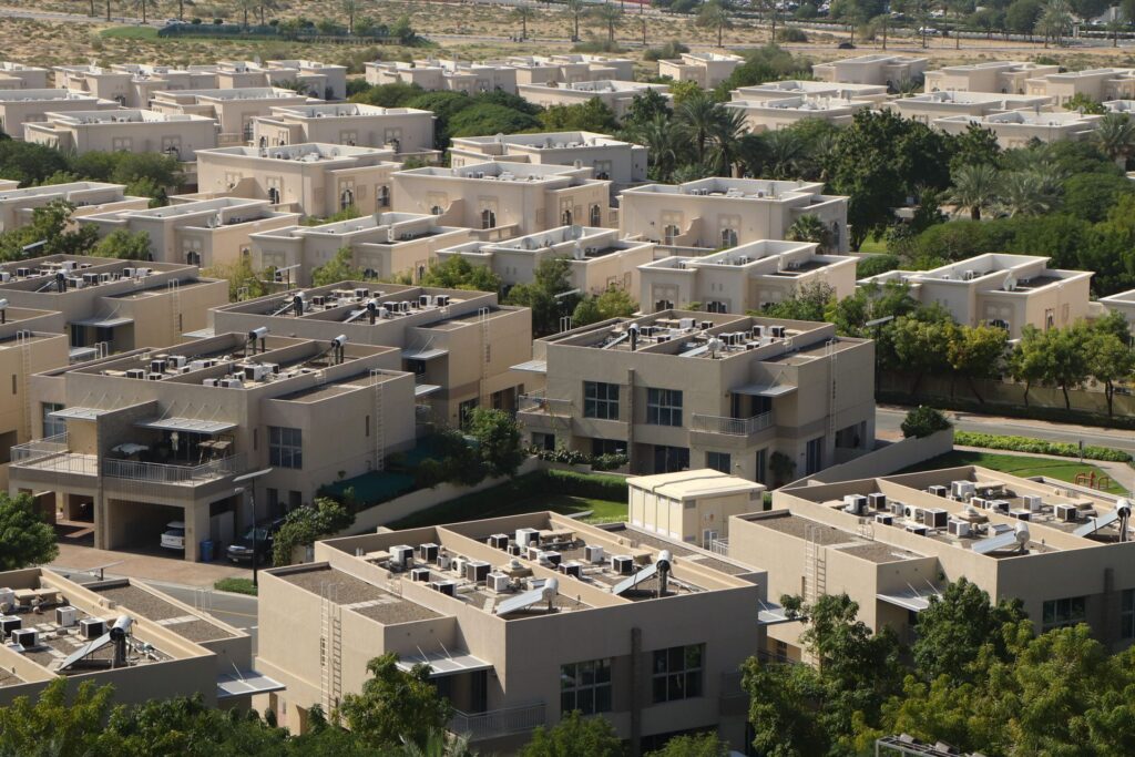 Aerial view of a dense Dubai villa and townhouse community with sand-toned architecture and palm trees, representative of The Valley by Emaar's neighbourhoods