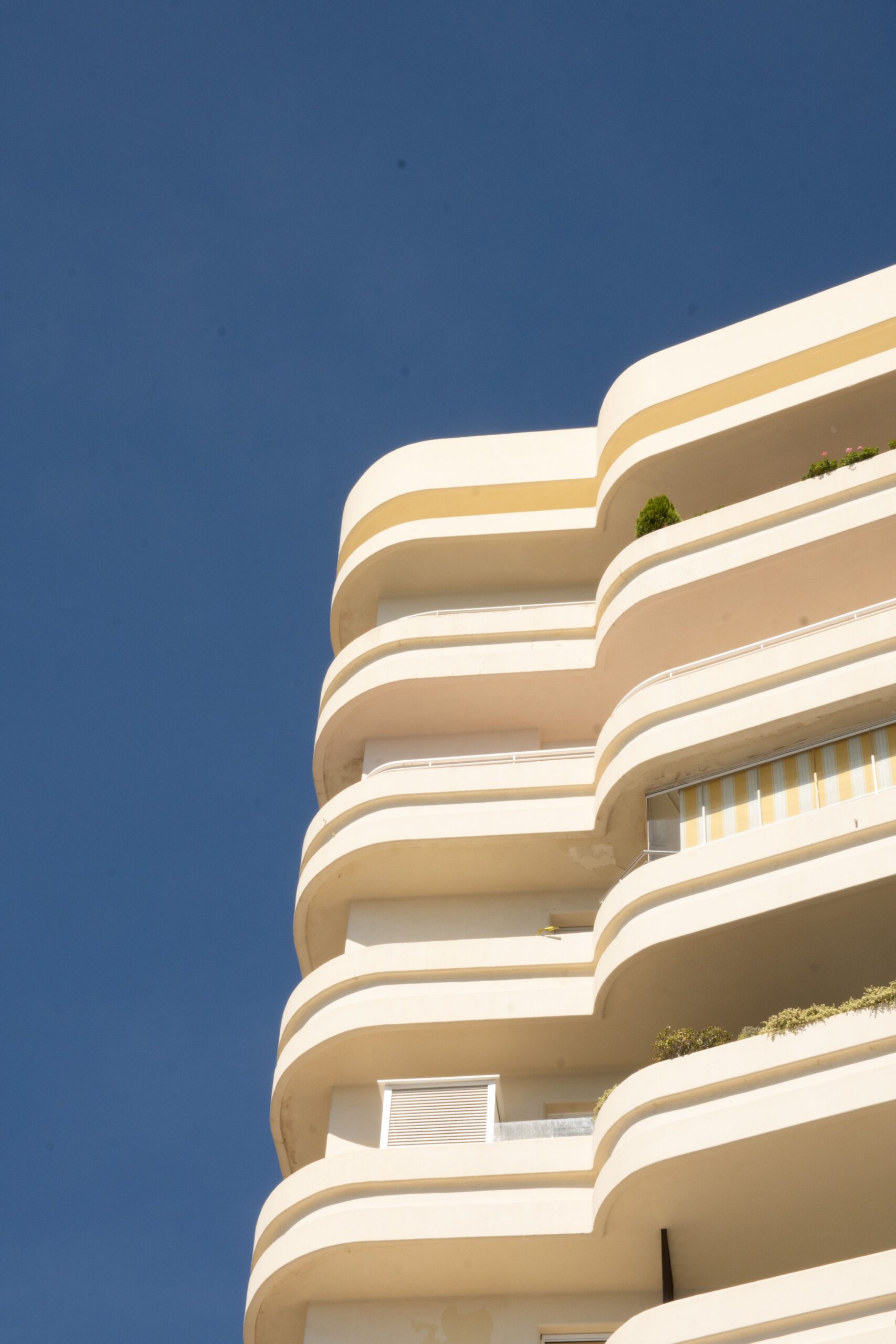 Low angle view of a modern apartment building with curved cream balconies against a clear blue sky in Dubai