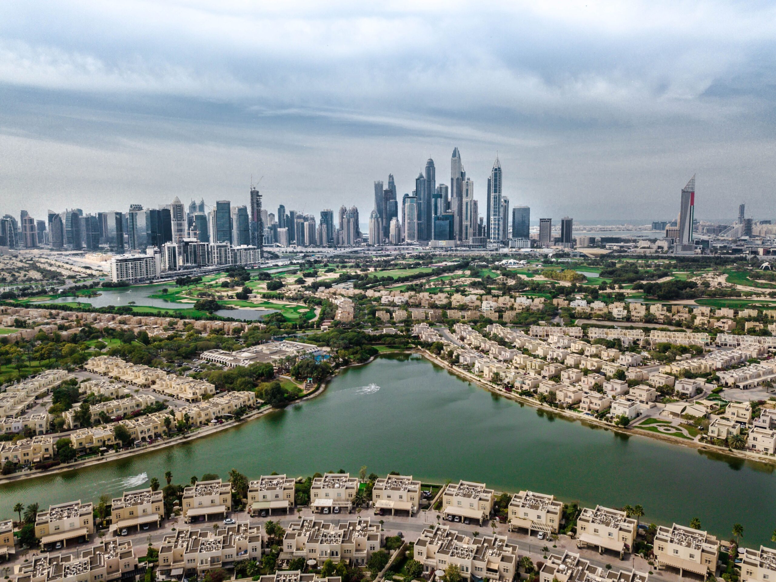 Aerial view of a Dubai golf course and low-rise villa community with the city skyline in the background