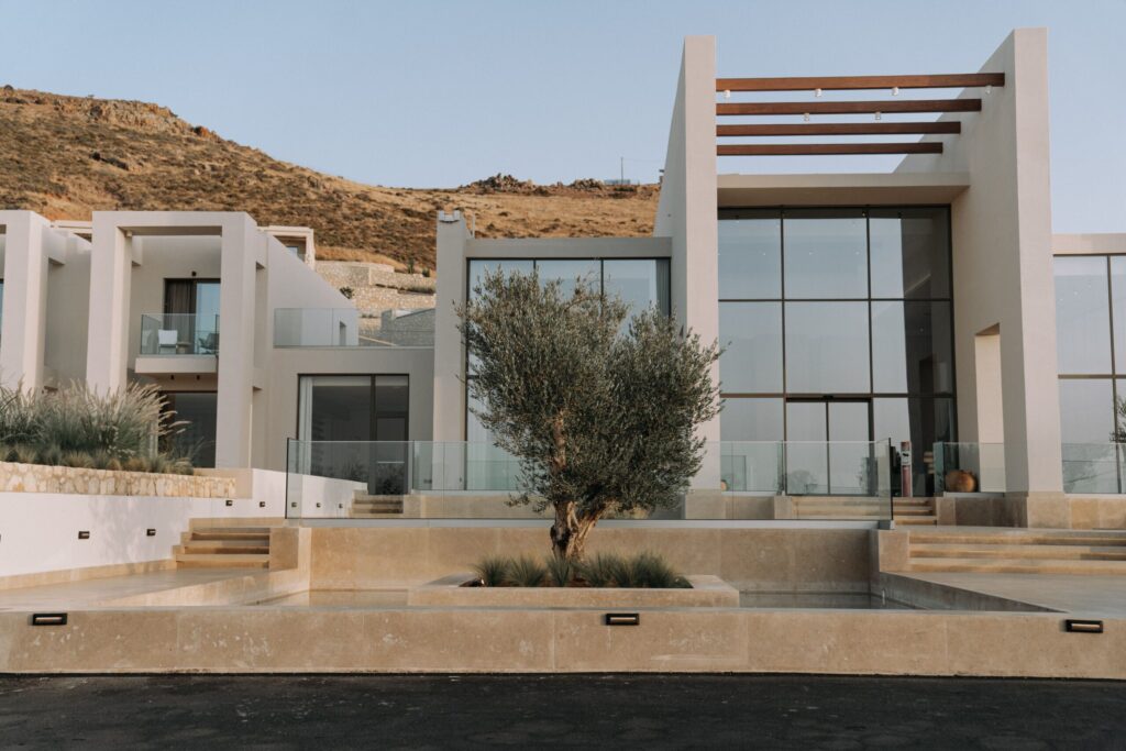 Modern flat-roof villa with glass facade and stone terrace against a sandy hillside, representative of the modern architectural style at Fairway Vistas, Dubai Hills Estate