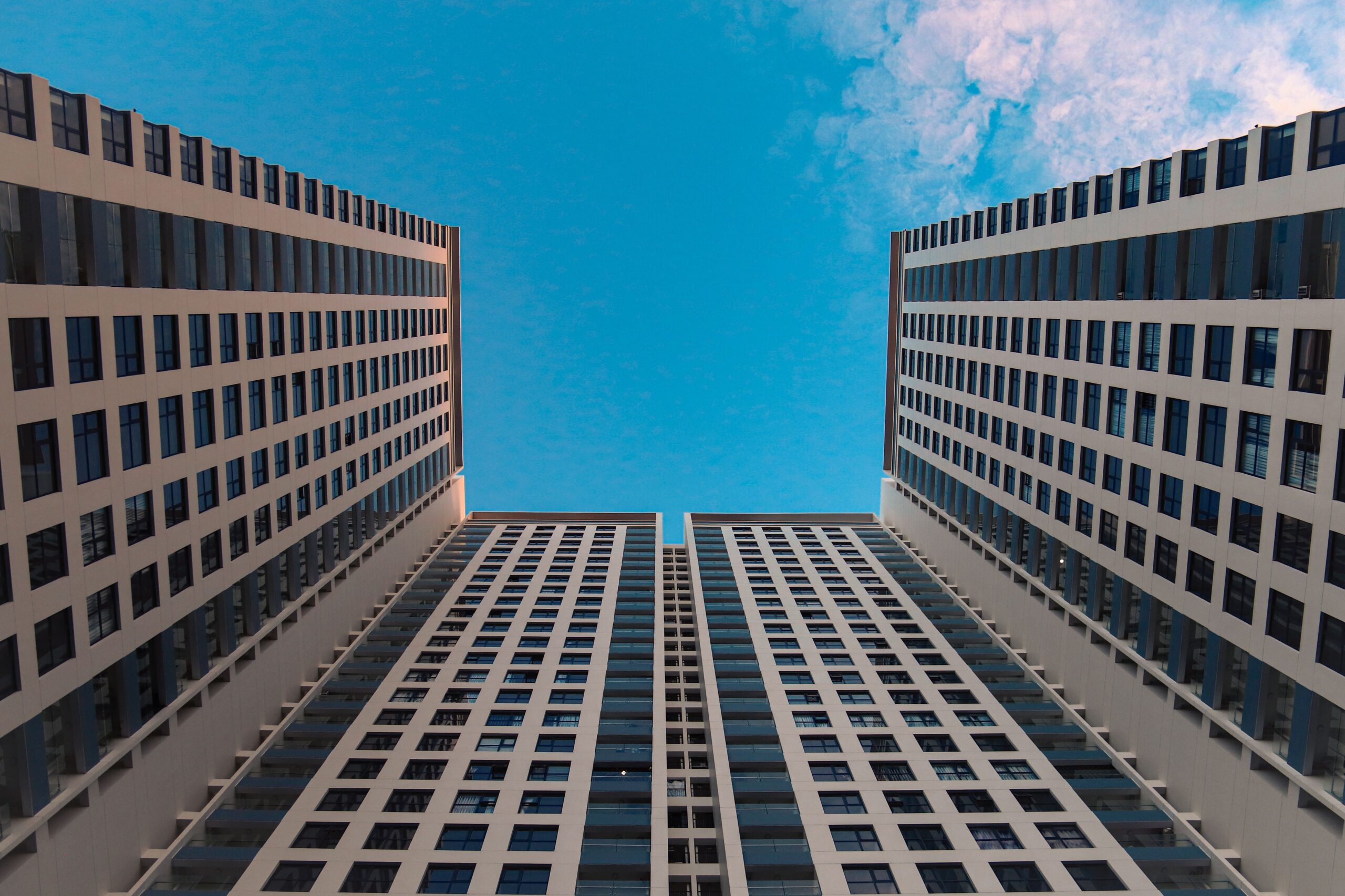 Two tall, symmetrical, grid-pattern modern residential towers converging toward a clear blue sky, representative of Geepas Residential Tower, Arjan
