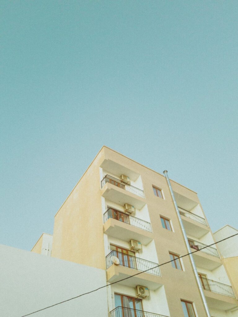 Cream-colored low-rise apartment building with balconies against a clear sky in a Gulf residential setting