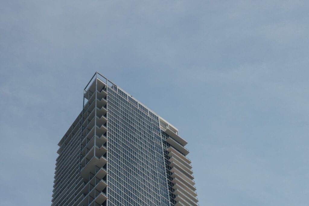 Low-angle view of a modern glass residential tower with balconies against a clear blue sky near O2 Tower, JVC