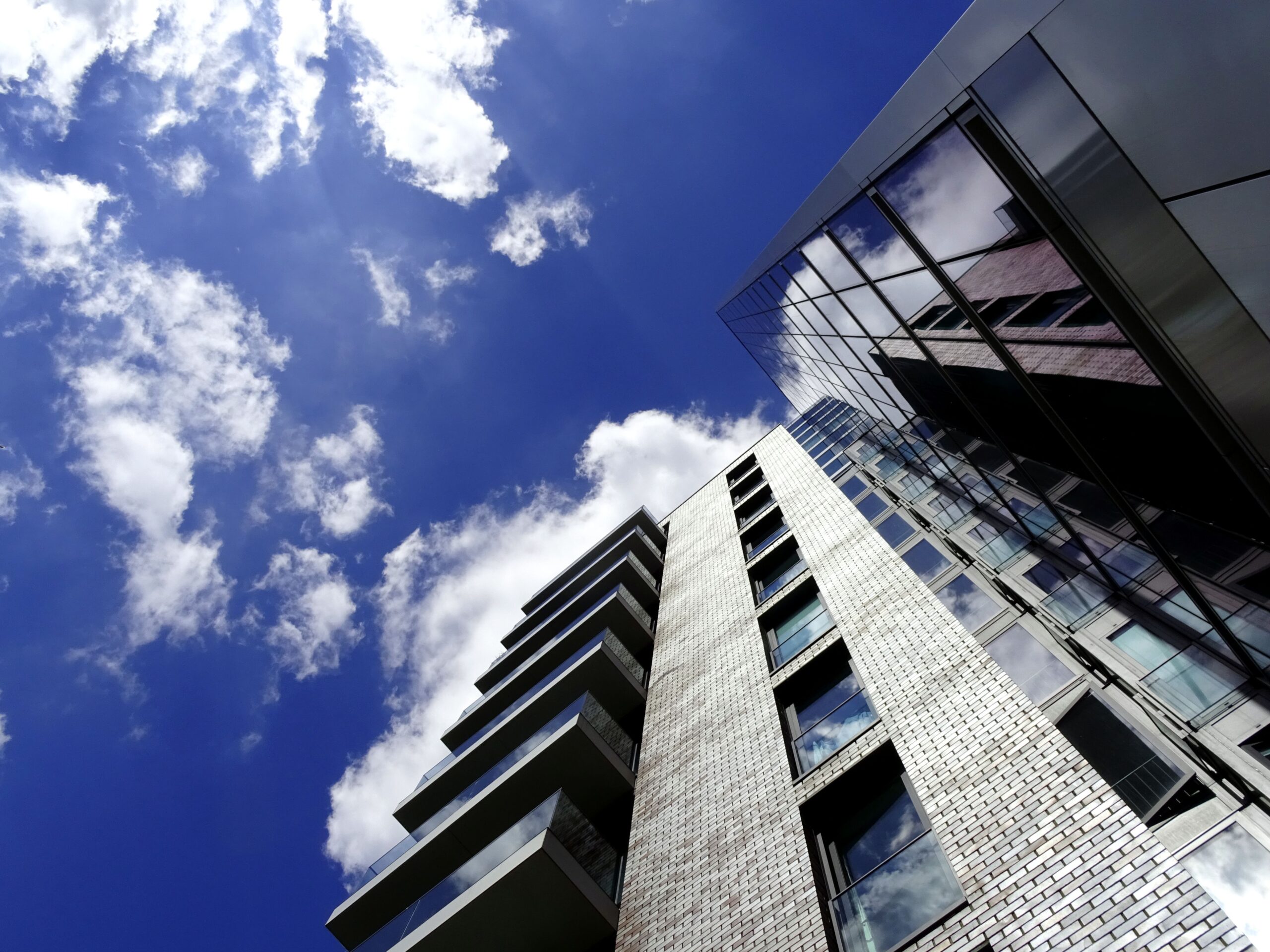 Modern residential tower with glazed balconies seen from below against a blue sky