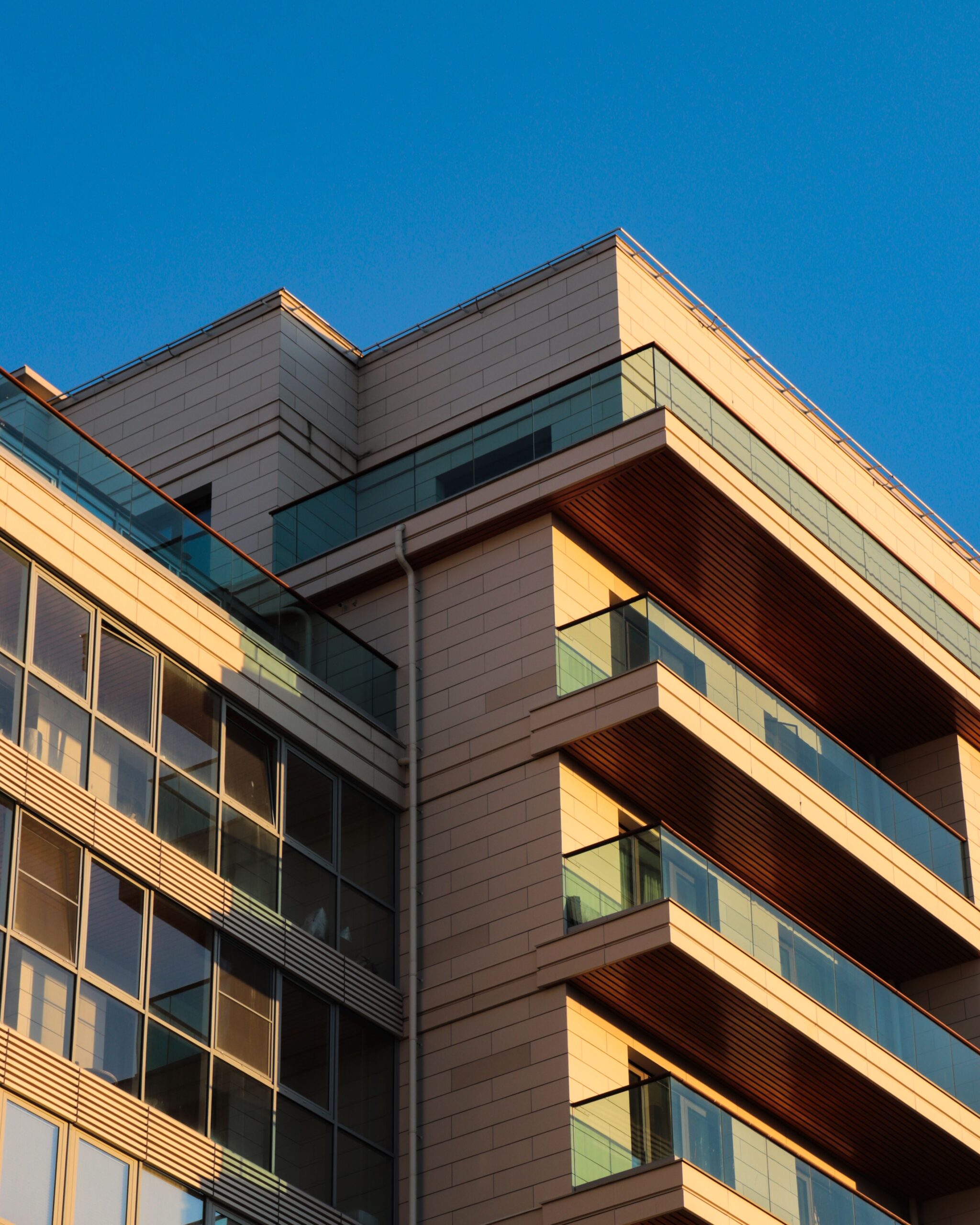 Modern apartment building corner with glass balconies lit by warm sunlight under a clear sky, representative of Binghatti Views in Dubai Silicon Oasis, Dubai