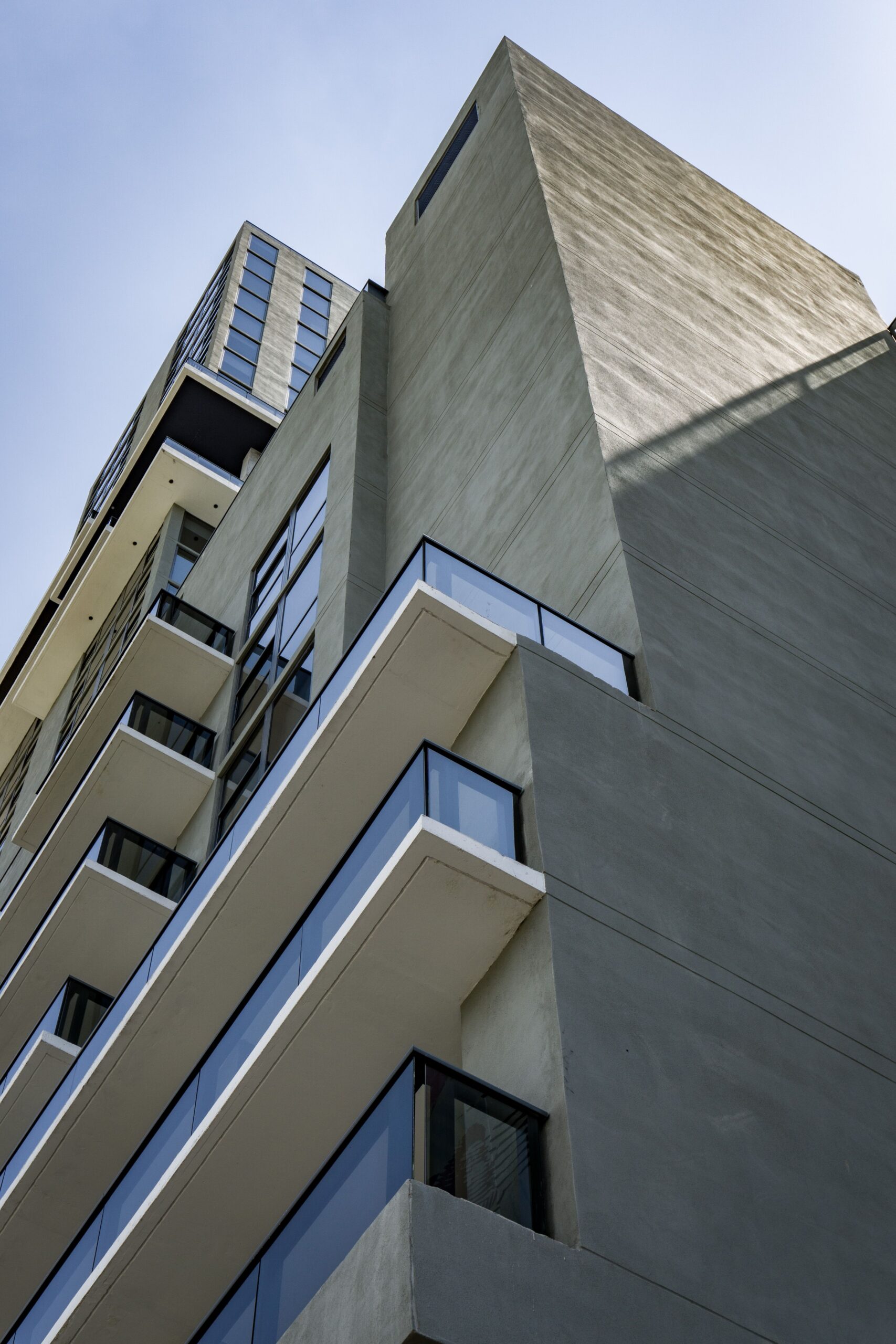 Low angle view of a modern cream apartment building corner with box balconies against a clear blue sky in Dubai