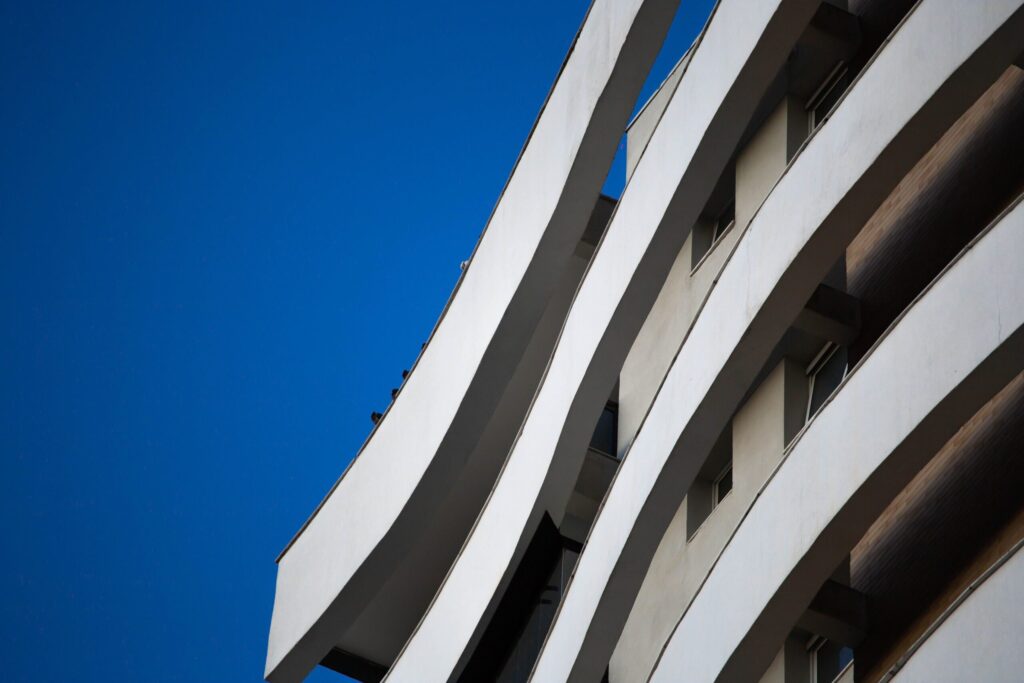 Close-up low-angle view of a modern building's curved white balcony forms against a clear blue sky, representative of Westwood by Imtiaz in Al Furjan, Dubai
