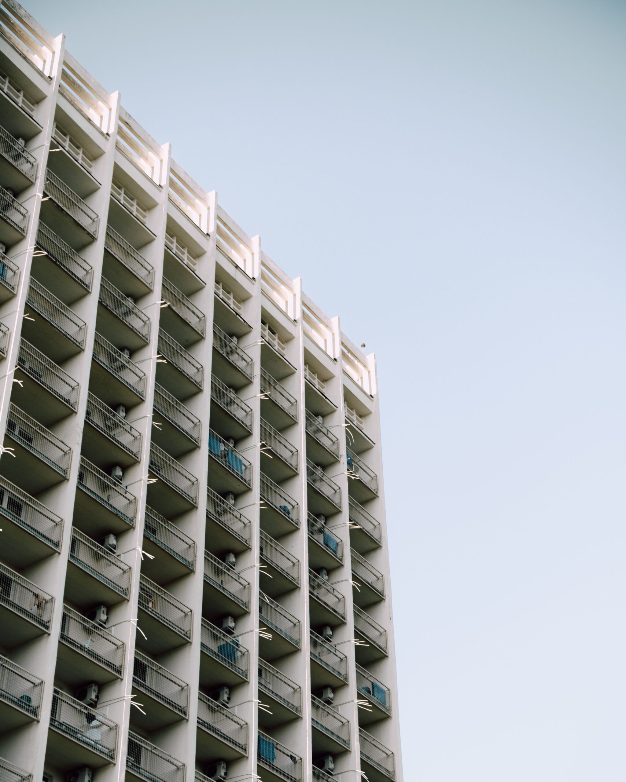 Low-angle view of a modern Dubai apartment tower with a regular balcony grid pattern against a clear blue sky