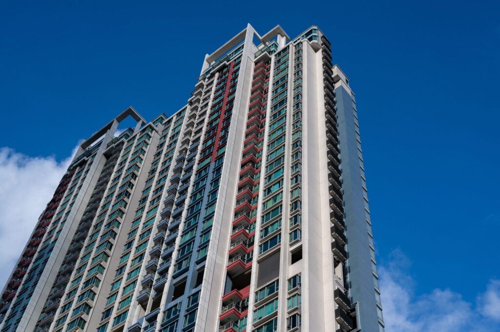 Tall residential tower with white and red-trimmed balconies against a deep blue sky
