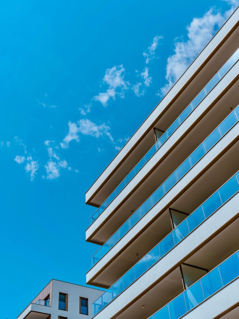 Low angle view of a modern apartment building's white balconies with glass railings against a blue sky with light clouds in Dubai