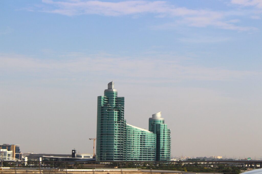Two tall, symmetrical, green-glass modern residential towers against a clear blue sky, representative of Genesis by Meraki, Arjan