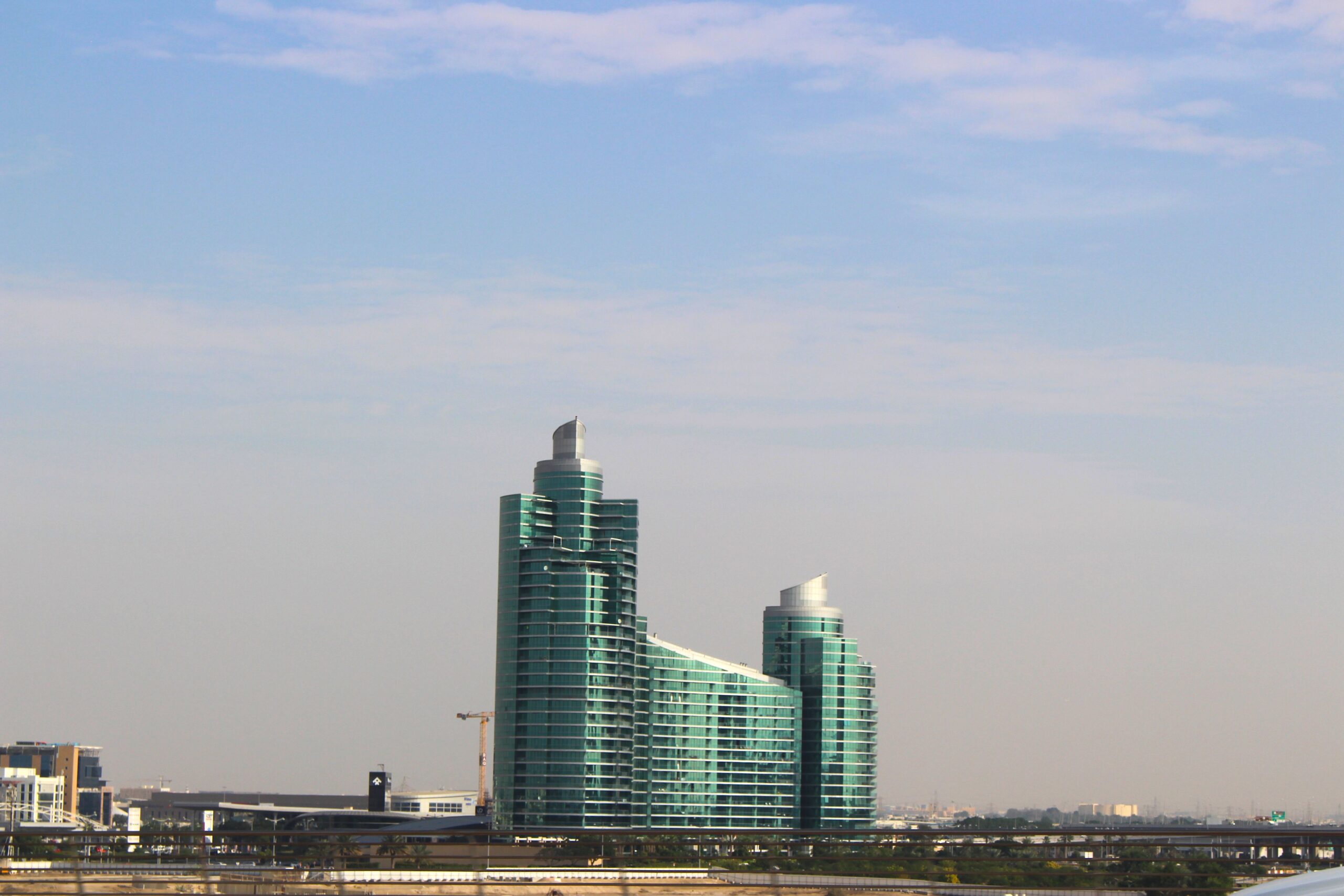 Two tall, symmetrical, green-glass modern residential towers against a clear blue sky, representative of Genesis by Meraki, Arjan