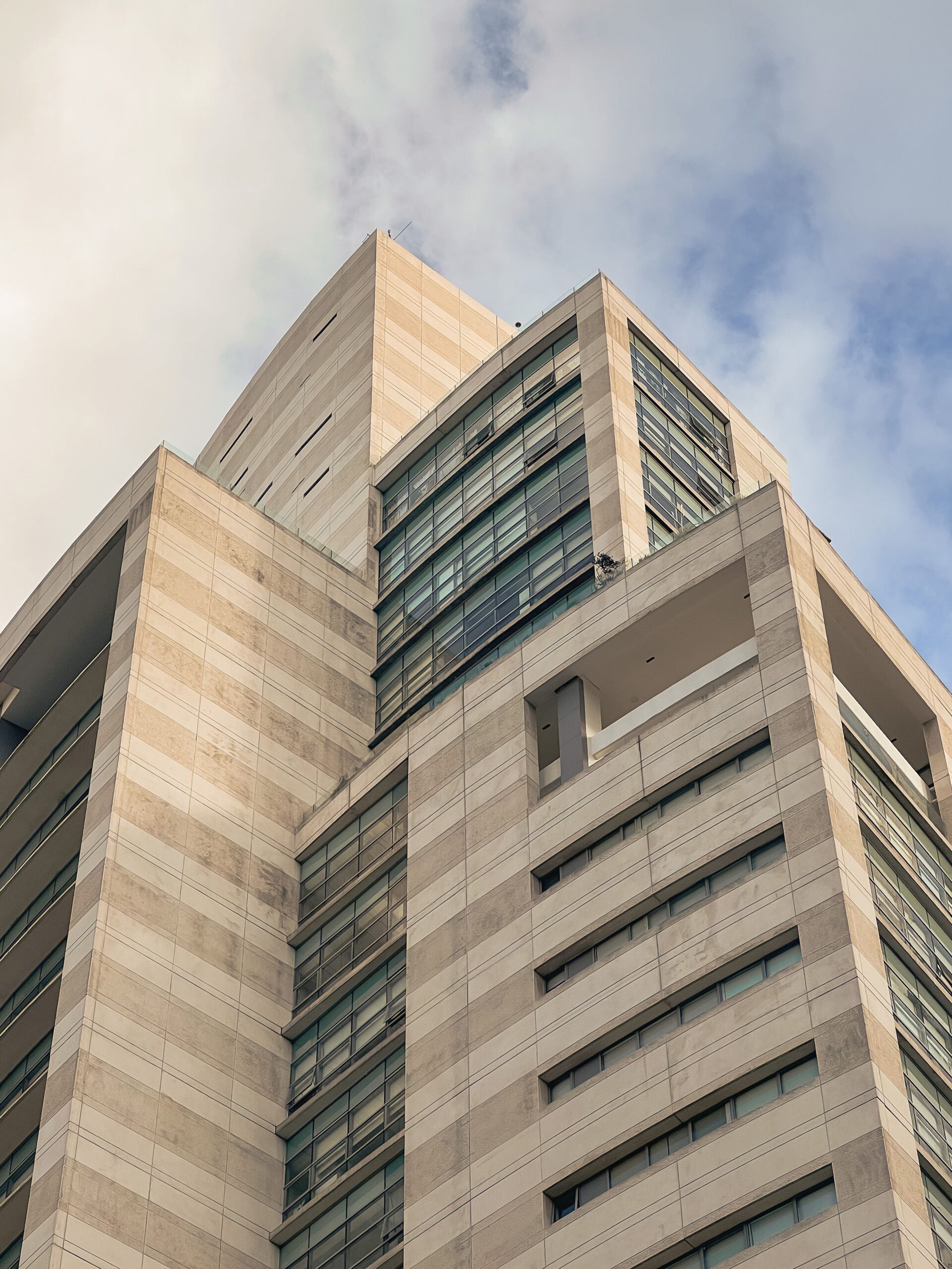 Upward angled view of a modern high-rise apartment building with a tan stone and glass facade in Dubai