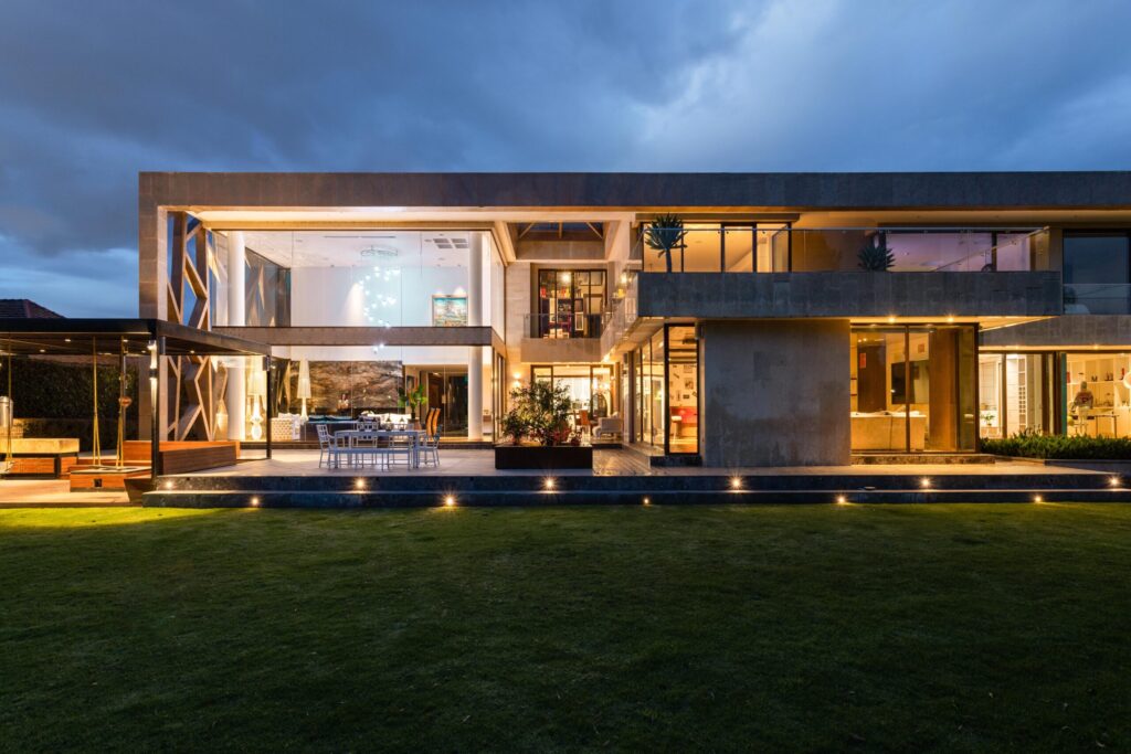 Modern contemporary villa exterior illuminated at dusk with glass facade and landscaped lawn, representative of a Dubai Hills Estate villa community near Dubai Hills View