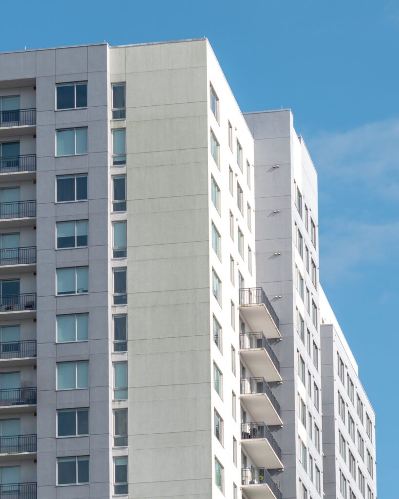 Close-up corner view of a modern Dubai residential building with light precast facade and railed balconies, representative of Sondos Sage in DubaiLand Residence Complex, Dubai