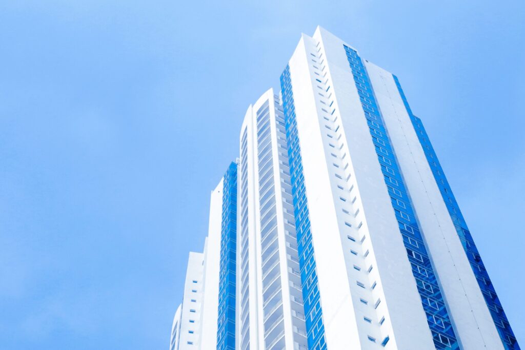 White residential tower with blue accent stripes rising into a bright blue sky