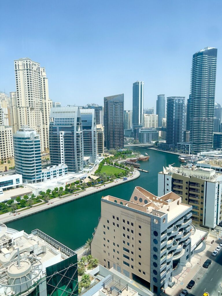 Aerial daytime view of Dubai Marina's waterfront towers and canal promenade lined with palm trees and boats