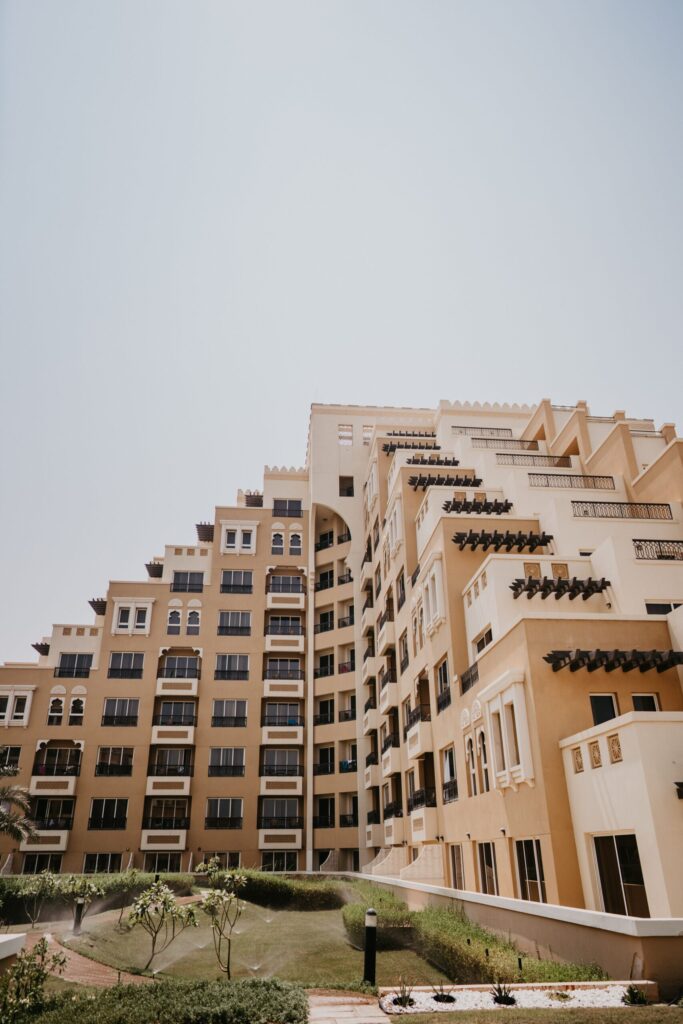 Mid-rise Arabic-style residential apartment building with balconies and landscaped garden foreground under a clear Dubai sky, representative of Azizi Daisy in Al Furjan