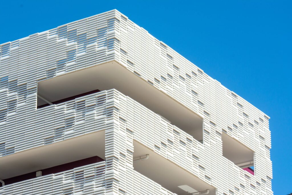 Close-up corner view of a modern white ribbed low-rise building facade against a clear blue sky, no people, no branding