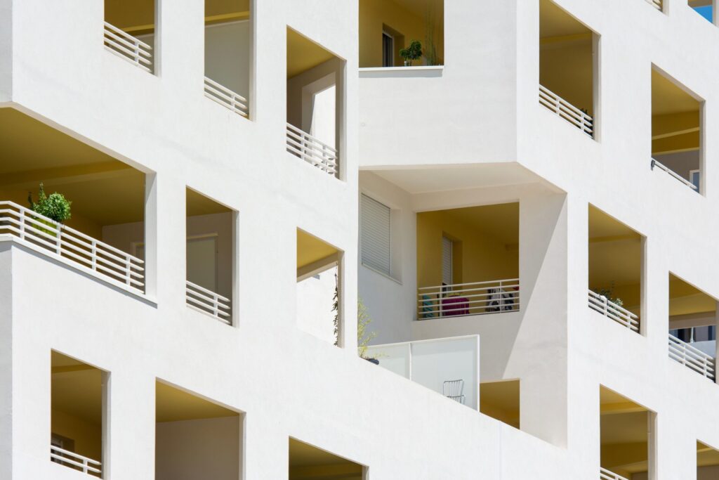 White modern apartment facade with recessed balconies and white railings in strong sunlight
