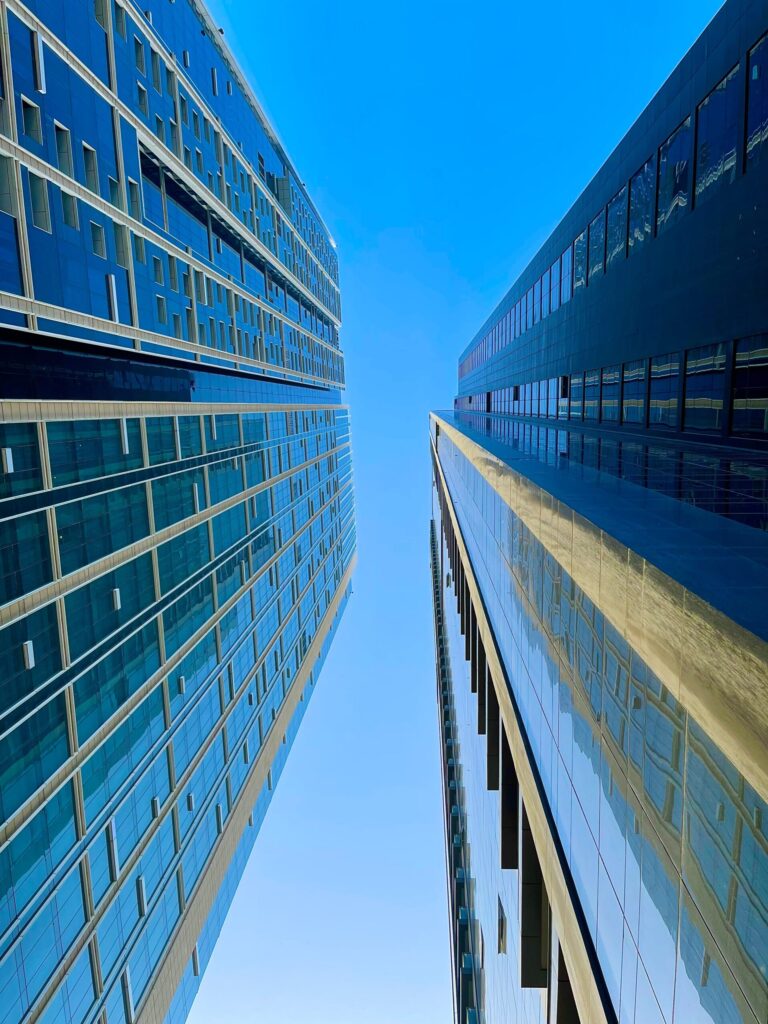 Dramatic upward view between two blue-glass high-rise towers in Dubai Marina under a clear sky