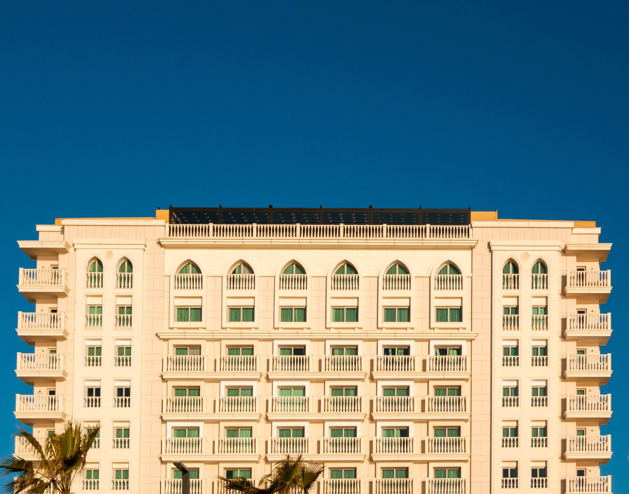 Cream-coloured mid-rise apartment building with arched windows and white balconies under a deep blue sky