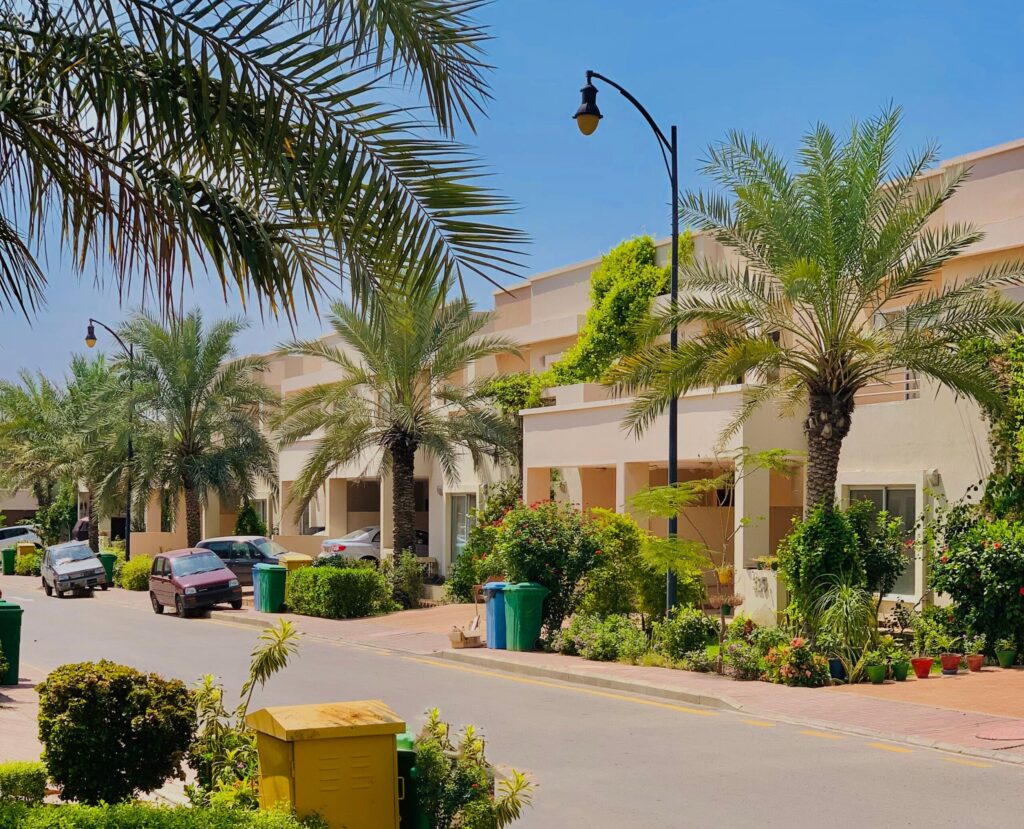 Row of townhouses along a palm-lined residential street with parked cars, similar to Sobha Hartland Estates, Sobha Hartland