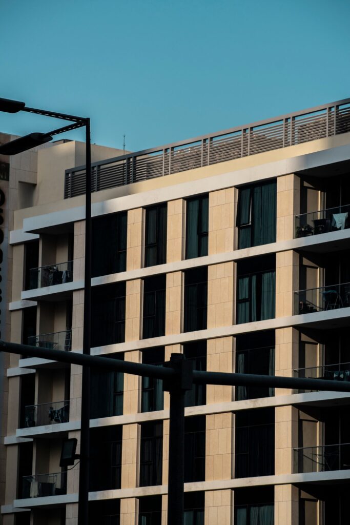 Sunlit facade of a modern cream-toned mid-rise Dubai apartment building with glass balconies, representative of a Town Square, DubaiLand residential building
