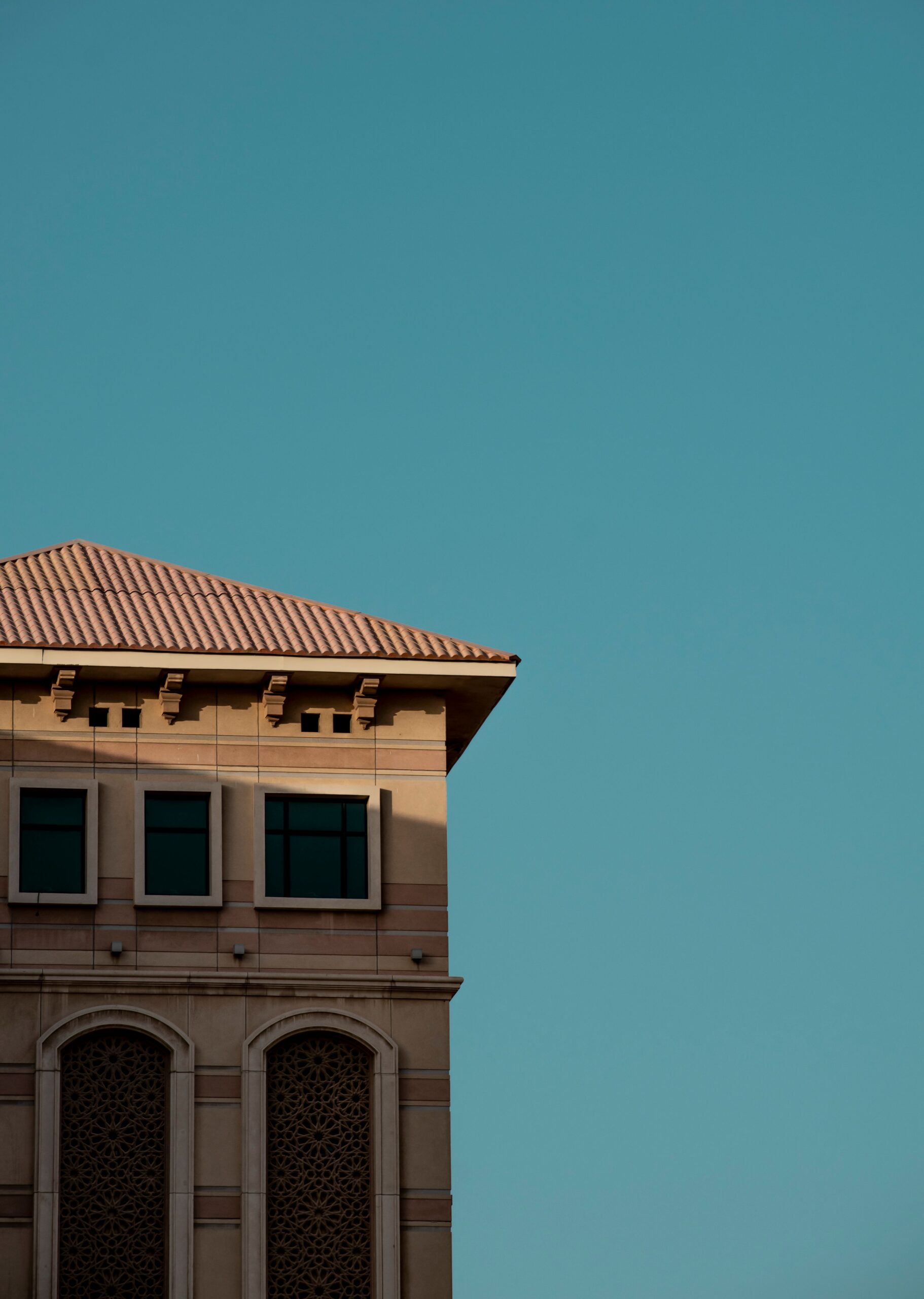 Cream-facade Mediterranean-style apartment building corner with a terracotta tile roof and arched windows under a clear blue sky in Dubai, representative of Azizi Liatris's residential architecture in Al Furjan