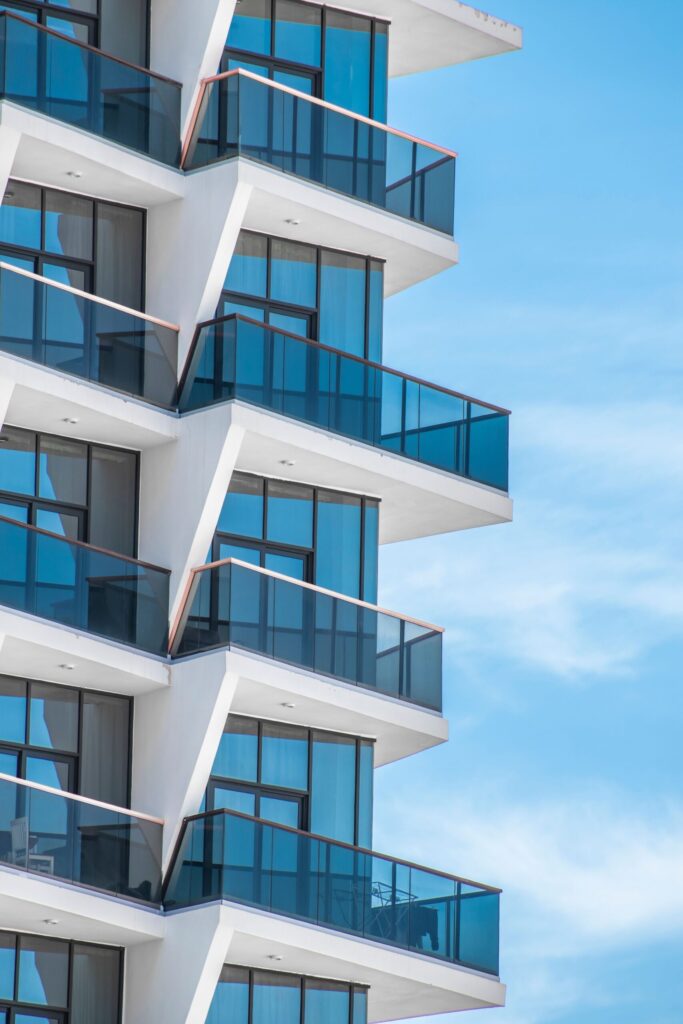 Modern white and glass residential high-rise with zig-zag balconies against a clear blue sky, representative of Azizi Freesia in Al Furjan, Dubai