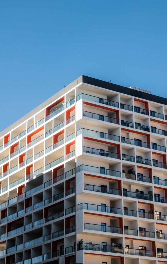 Orange and white high-rise apartment building with balconies under a clear blue sky, Dubai