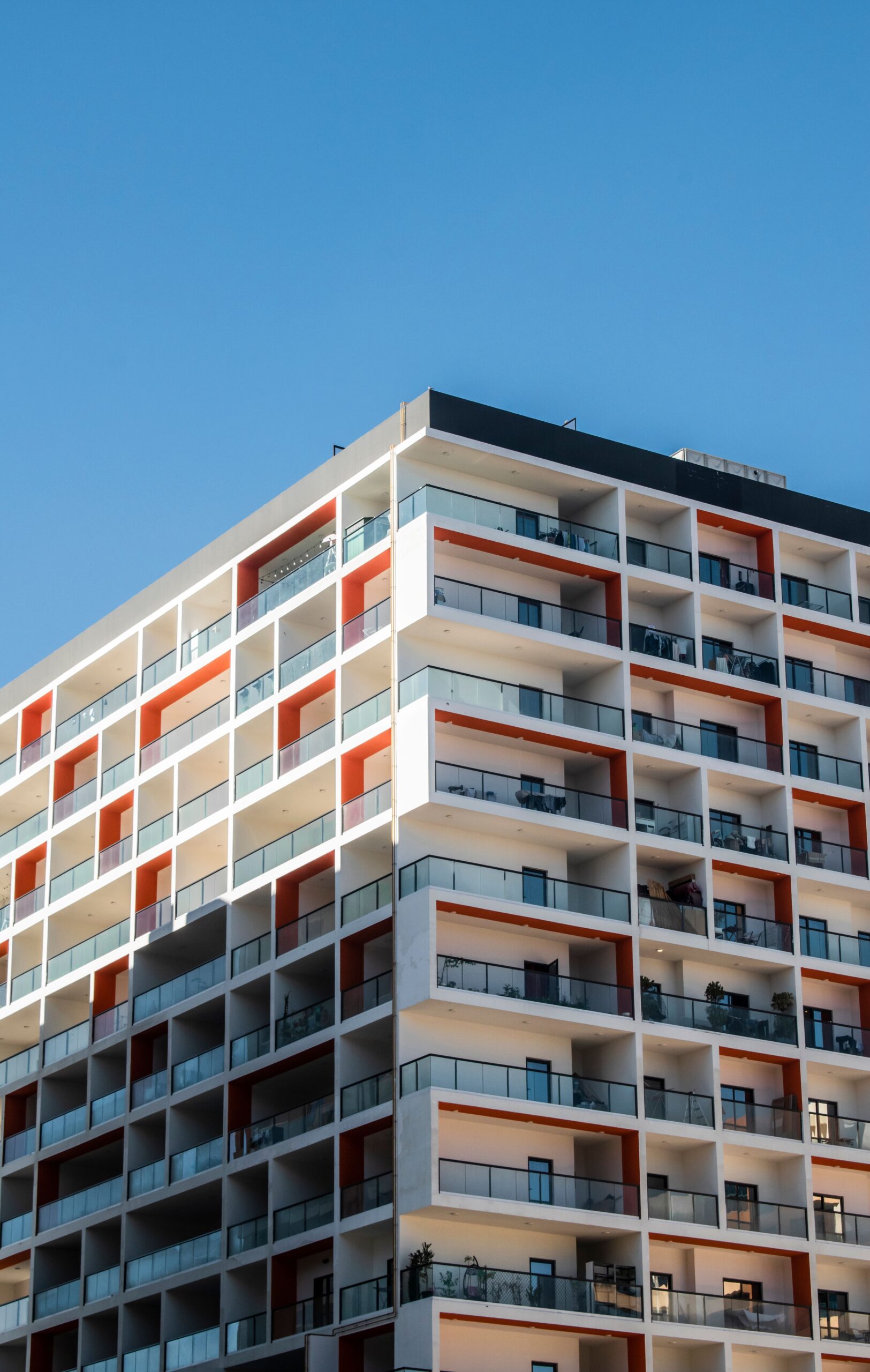 Orange and white high-rise apartment building with balconies under a clear blue sky, Dubai