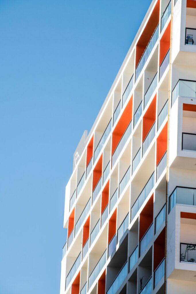 Close-up corner view of a modern Dubai apartment building facade with white and orange checkerboard balconies, representative of Binghatti West in DubaiLand Residence Complex, Dubai