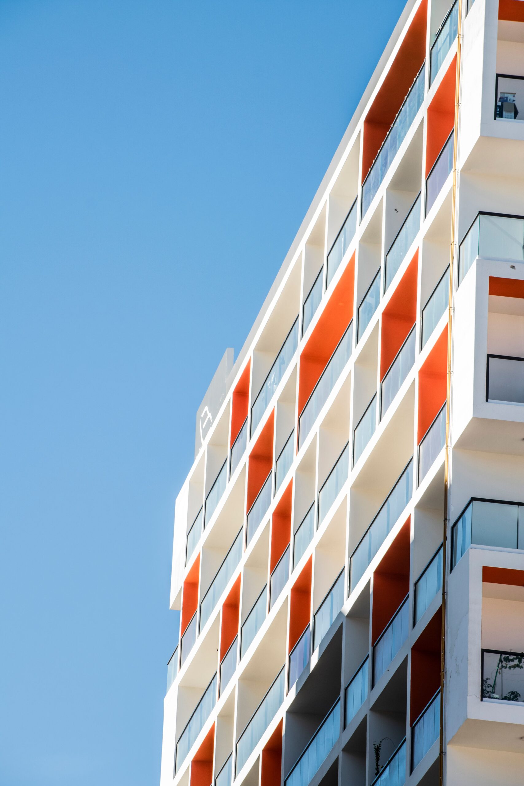 Close-up corner view of a modern Dubai apartment building facade with white and orange checkerboard balconies, representative of Binghatti West in DubaiLand Residence Complex, Dubai