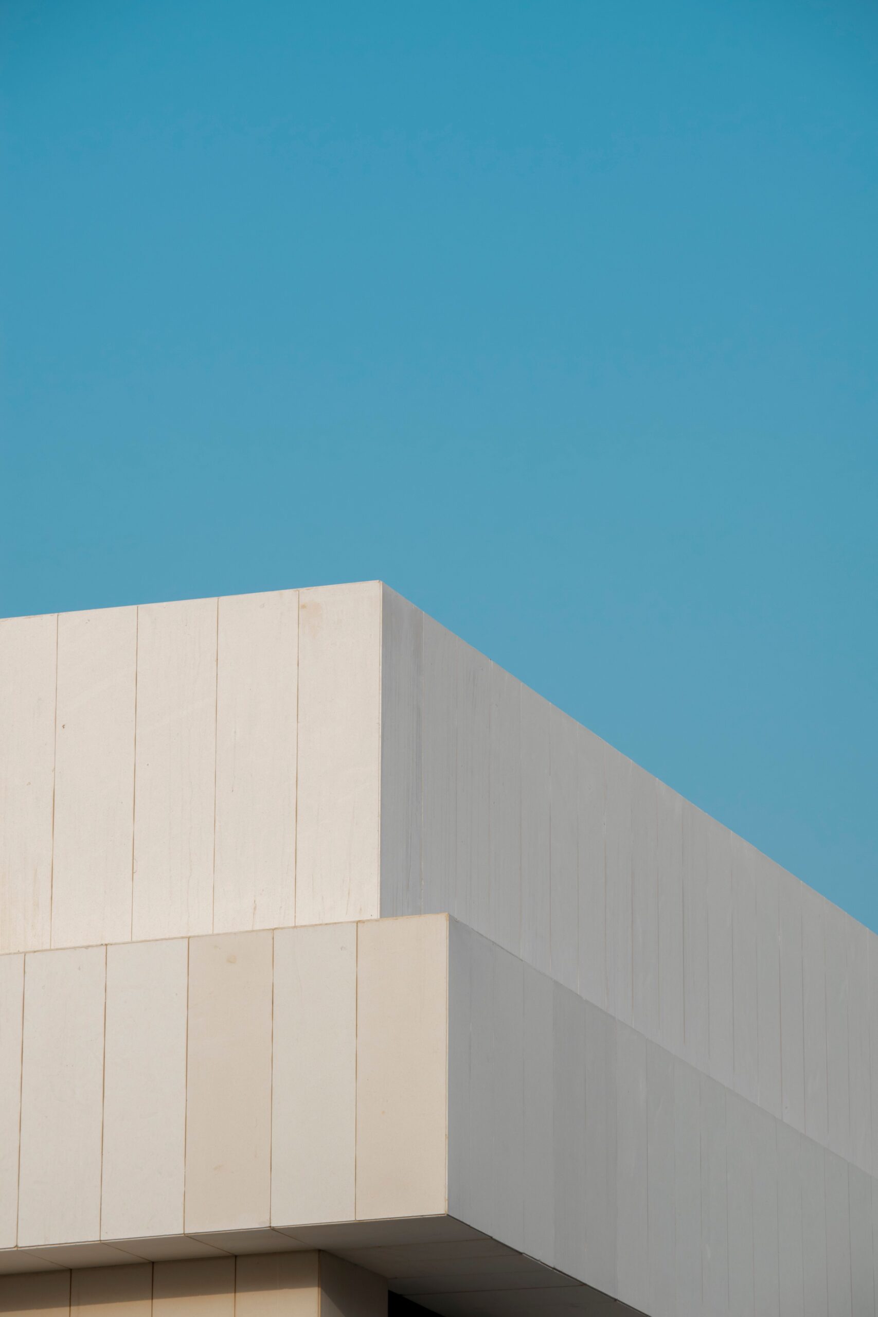 Clean minimalist white apartment building corner against a clear blue sky, similar in style to Orchid, DAMAC Hills
