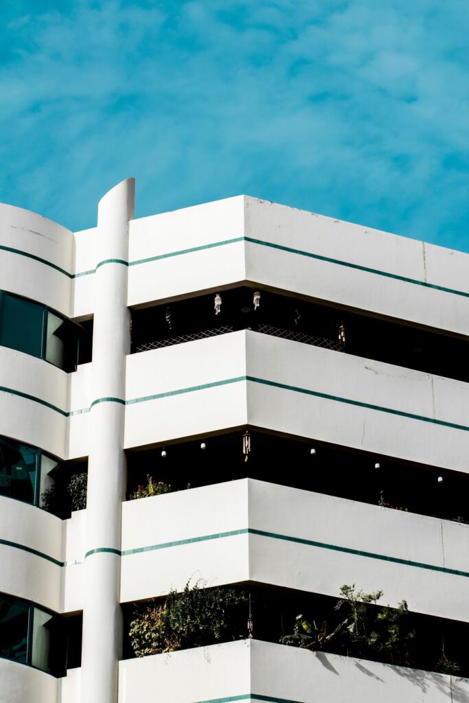 Corner of a white mid-rise apartment building with teal accent stripes against a clear blue sky in Dubai