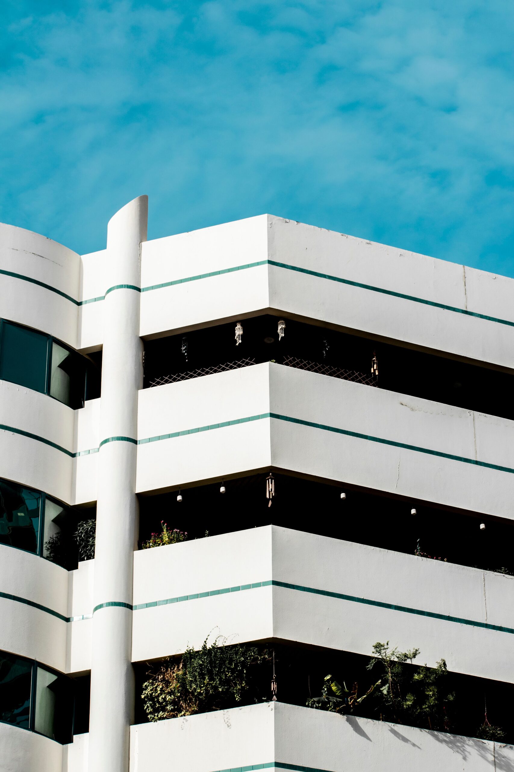 Corner of a white mid-rise apartment building with teal accent stripes against a clear blue sky in Dubai