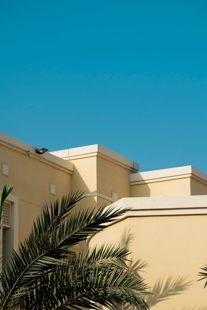 Cream-coloured Dubai building parapet against a deep blue sky with a palm frond in the foreground, representative of Luna Residence in DubaiLand Residence Complex