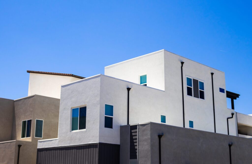 Minimalist modern apartment building exterior in muted white and grey stucco under a clear blue sky, representative of Taraf 2 Residence's contemporary low-rise architecture in JVT